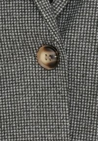 Close-up af en brun, firehullet knap på sort- og hvidternet stof med hundetandsmønster, sandsynligvis en del af en frakke eller jakke.