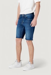 Shorts de mezclilla en azul oscuro con un diseño clásico de cinco bolsillos, dobladillos enrollados y un ajuste slim, combinados con zapatillas blancas.
