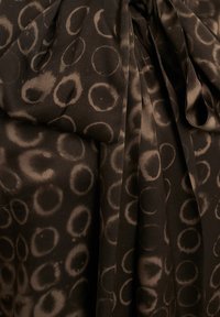 Tessuto marrone a motivo con motivi circolari in marrone chiaro, con una finitura satinata e design drappeggiato, che mette in mostra una texture morbida e un movimento fluido.