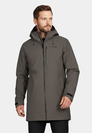 Mężczyzna w szarej wodoodpornej kurtce z kapturem, z zapięciem na zamek z przodu i kieszenią na piersi, stojący na tle białym.