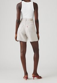 Vaaleanharmaat farkkushortsit, joissa on takataskut ja erottuva merkkietiketti; yhdistetty valkoiseen hihattomaan puseroon ja violetteihin korkokenkiin.