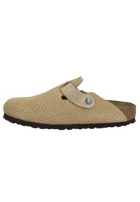 Sabots en suède beige à enfiler avec un design perforé, semelle en liège, sangle réglable et semelle en caoutchouc foncé. Avec un accent en métal logo.