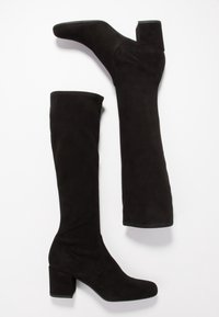 Botas de ante negras hasta la rodilla con tacón cuadrado, puntera afilada y textura suave. El eje presenta un diseño sin costuras y con un mínimo de costura.