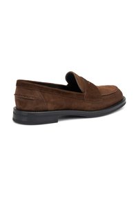 Mocasín de ante marrón, sin cordones, con punta redonda, suela plana de goma negra y costuras decorativas a lo largo de la parte superior para un detalle adicional.