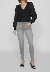 Suéter negro de cuello en v con mangas abullonadas en patrón de encaje, combinado con jeans skinny gris claro y tacones negros con tiras.