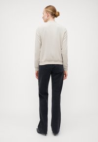 Světle béžová bomber bunda s hladkým povrchem, žebrované manžety a lem, spárovaná s černými kalhotami s vysokým pasem a elegantními černými botami.