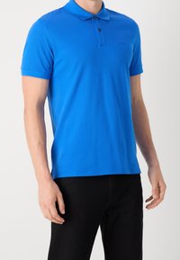 Modrá polo košile vyrobená z bavlny, s límečkem, krátkým rukávem a zapínáním na tři knoflíky, s rovnými liniemi a detailem loga.