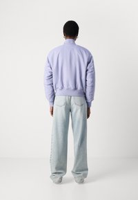 Svijetloljubičasti bomber s rebrastim manžetama i rubom, uparen s prevelikim svijetloplavim trapericama koje imaju ležeran kroj.