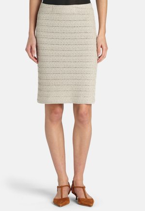 Beżowa dzianinowa ołówkowa spódnica za kolano, noszona z brązowymi czółenkami na cienkim pasku z przodu i czarną włożoną do środka bluzką.