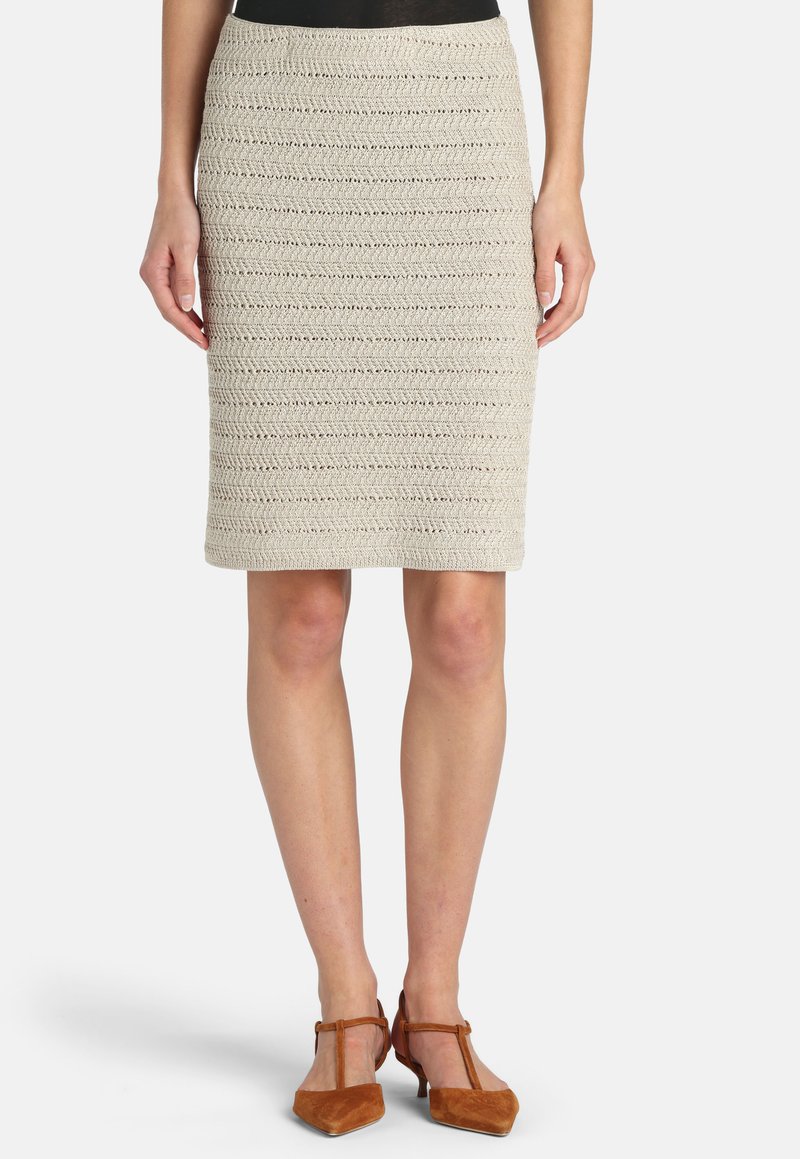 Jupe crayon beige en tricot atteignant les genoux, portée avec des talons à bout pointu brun à bride en T et un haut noir rentré.