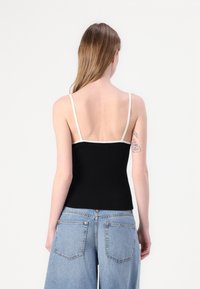 Svart ribbet singlet med tynne hvite stropper, med en tettsittende design og minimalistisk stil, kombinert med lyseblå jeans.