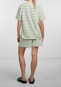 Conjunto de camiseta de manga corta a rayas y pantalones cortos en verde claro y blanco. Tejido suave, corte relajado y cuello redondo sencillo. Zapatos planos con correas.