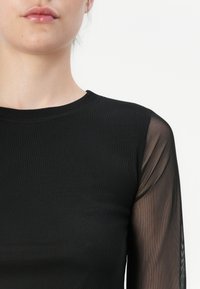Black long-sleeve top with a solid body and sheer mesh sleeves, featuring a crew neckline and a textured fabric.