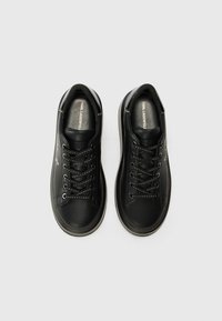 Baskets en cuir noir avec un design à lacets, des coutures blanches contrastantes, une pointe arrondie et une texture lisse. Logo visible sur la semelle intérieure.