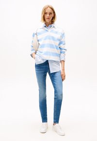 Šviesiai mėlynas ir baltas dryžuotas džemperis dėvimas ant melsvai dryžuoto marškinio, derinamas su aptemptais mėlynais džinsais ir baltais sportbačiais. Minimalistinė smėlio spalvos rankinė.