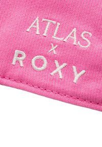 Tejido rosa con un tejido texturizado presenta bordado blanco que dice "ATLAS x ROXY". Se aprecian bordes limpios y detalles de costura.