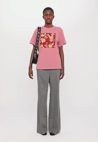 Rosa bomulls t-skjorte med et blomster grafisk design, sammen med grå, vide bukser laget av strukturert stoff, og en svart skulderveske.