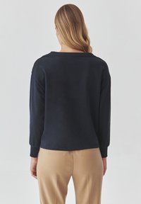 Dunkelblaues Sweatshirt mit langen Ärmeln und lockerer Passform, mit gerippten Bündchen und Kragen, von hinten gezeigt, kombiniert mit beigen Hosen.