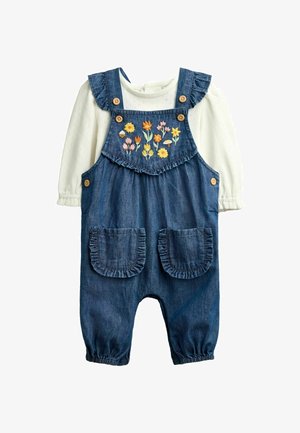 Hvid langærmet skjorte under blå denim-overalls med flæse-stropper, to frontlommer, træknapper og farverig blomsterbroderi.