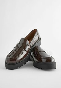 Paire de mocassins à plateforme marron foncé brillant avec semelles épaisses noires sur fond blanc.