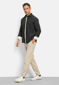 Dunkles Hemd mit Brusttasche, über einem hellen Hemd getragen, kombiniert mit beigen Cordhosen und weißen Turnschuhen, für einen entspannten Look.