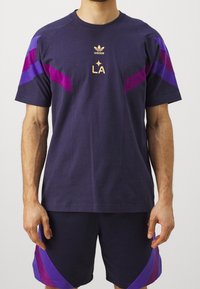 Marinblå sporttröja med lila detaljer, med rund halsringning, korta ärmar och "LA"-logotyp i guld. Matchas med matchande shorts.