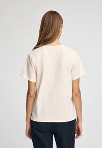 Camiseta de manga corta de color crema hecha de algodón, con cuello redondo y un corte relajado, con costuras mínimas y sin patrones visibles.