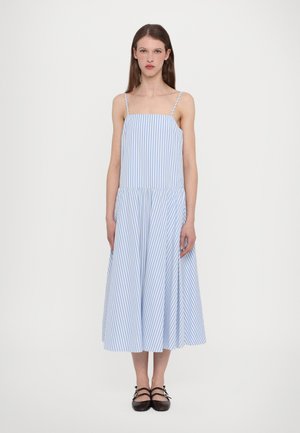 Gestreiftes Leinenkleid mit dünnen Trägern, einem taillierten Oberteil und einem schwingenden, knielangen Rock in Hellblau und Weiß. Schwarze flache Schuhe.