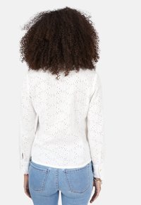 Hvid langærmet bluse med tekstureret stof, subtile striber og broderede detaljer. Har knapdetaljer ved manchetter. Båret med lyseblå jeans.