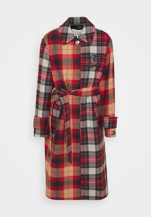 Long manteau à carreaux avec motif rouge, noir, beige et blanc, taille ceinturée, col boutonné et manches longues avec détails aux poignets.