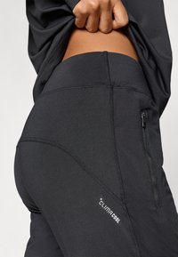 Čierne športové nohavice s priliehavým strihom, vybavené zipsovým vreckom, kontrastným prešívaním a malým logom "climacool" na boku.