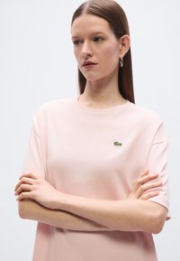 Ροζ κοντομάνικο μπλουζάκι από μαλακό ύφασμα, με μικρό πράσινο λογότυπο κροκόδειλου στο στήθος. Απλή, άνετη γραμμή.