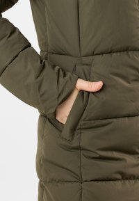 Olijfgroen pufferjack met een gewatteerde structuur; voorzien van een zijzak en een duimopening in de mouw voor extra functionaliteit.