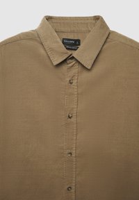 Camicia in velluto a coste color senape con vestibilità regolare, caratterizzata da un colletto a punta, chiusura frontale con bottoni e trama verticale a costine.