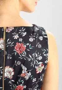 Blommönstrad klänning med svart bakgrund, prydd med färgglada pioner och fåglar, dragkedjedetalj på baksidan och slät textur.