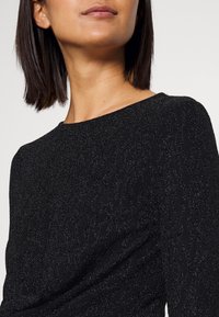 Top nero con texture che presenta un delicato motivo a onde, con scollo rotondo e una leggera lucentezza. Il tessuto liscio esalta l'eleganza del design.