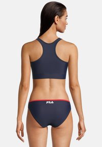 Marineblauw sportieve bikini-top met een racerback ontwerp, gecombineerd met bijpassende broekjes met een rode accentband en een opvallend logo op de achterkant.