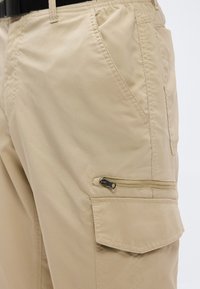 Μπεζ παντελόνια cargo από ελαφρύ ύφασμα, με πλαϊνές τσέπες και μια τσέπη με φερμουάρ στον μηρό, με ελαστική μέση.