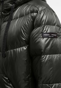 Padded green jacket featuring glossy, quilted fabric, adjustable drawstring hood, and a black fabric label with white logo on the sleeve.
