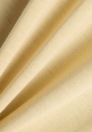 Zachte, lichtbeige stof met een fijne gebreide textuur, diagonaal gevouwen waardoor zachte schaduwen en hooglichten ontstaan.