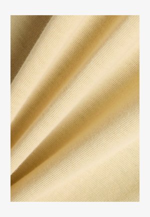 Zachte, lichtbeige stof met een fijne gebreide textuur, diagonaal gevouwen waardoor zachte schaduwen en hooglichten ontstaan.