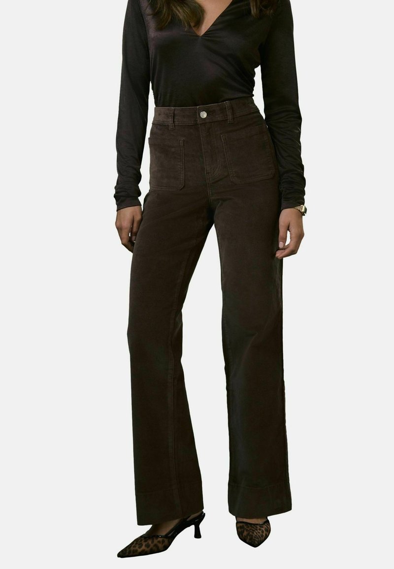 Pantalones de pana marrón de cintura alta con piernas anchas, bolsillos frontales y una textura suave, combinados con tacones negros puntiagudos con un patrón de leopardo.