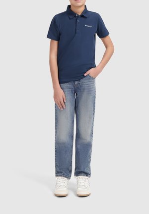 Marineblaues Poloshirt mit Kragen und Knopfleiste vorne, kombiniert mit hellblauen, verwaschenen Jeans und weißen Sneakern.