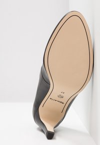 Chaussure à talon haut noire en cuir avec bout pointu, montrant une semelle beige lisse avec un fin contour noir et la taille 37.