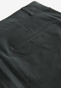 Crne hlače s glatkom teksturom, s jednim stražnjim džepom, šivenim detaljima i petljom za remen na struku.