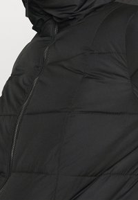Chaleco negro tipo puffer con cuello alto, patrón acolchado y cremallera frontal completa. Fabricado en un material sintético suave y brillante.