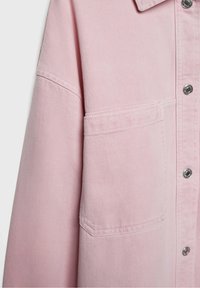 Chaqueta de mezclilla rosa claro con un bolsillo en el pecho, cierre de botones a presión y un acabado de tela texturizada, con detalles de costura sutiles.