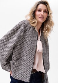 Bomberka w wzór houndstooth w czerni i bieli, z kremowym dekoltem i beżową bluzką pod spodem. Posiada kieszeń oraz ozdobny guzik.