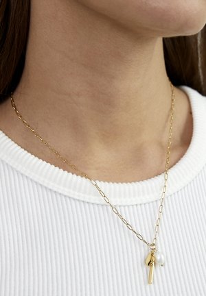 Goldkette mit ovalen Gliedern, versehen mit einer Perle und einem blattförmigen Anhänger, präsentiert vor einem strukturierten weißen Stoff.
