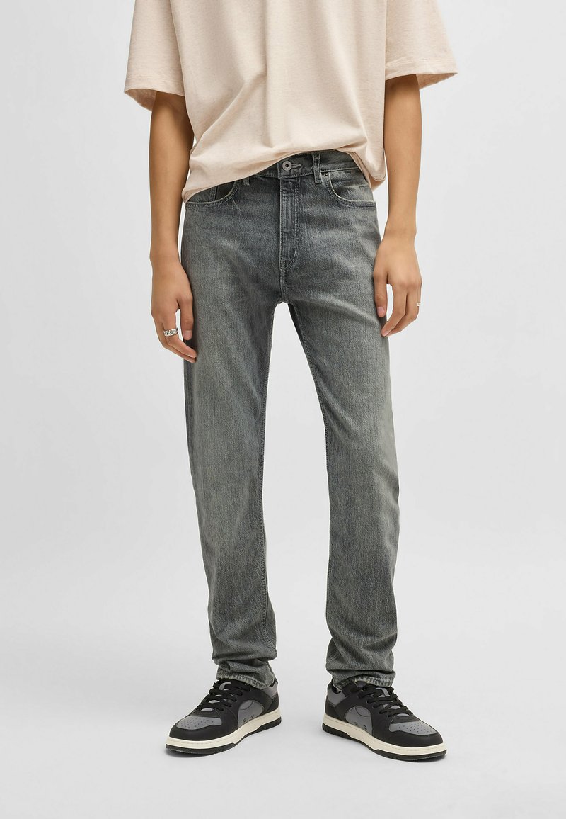 Grå denimjeans med rak passform, med blekt mönster och femficksdesign, tillsammans med svarta och grå sneakers.